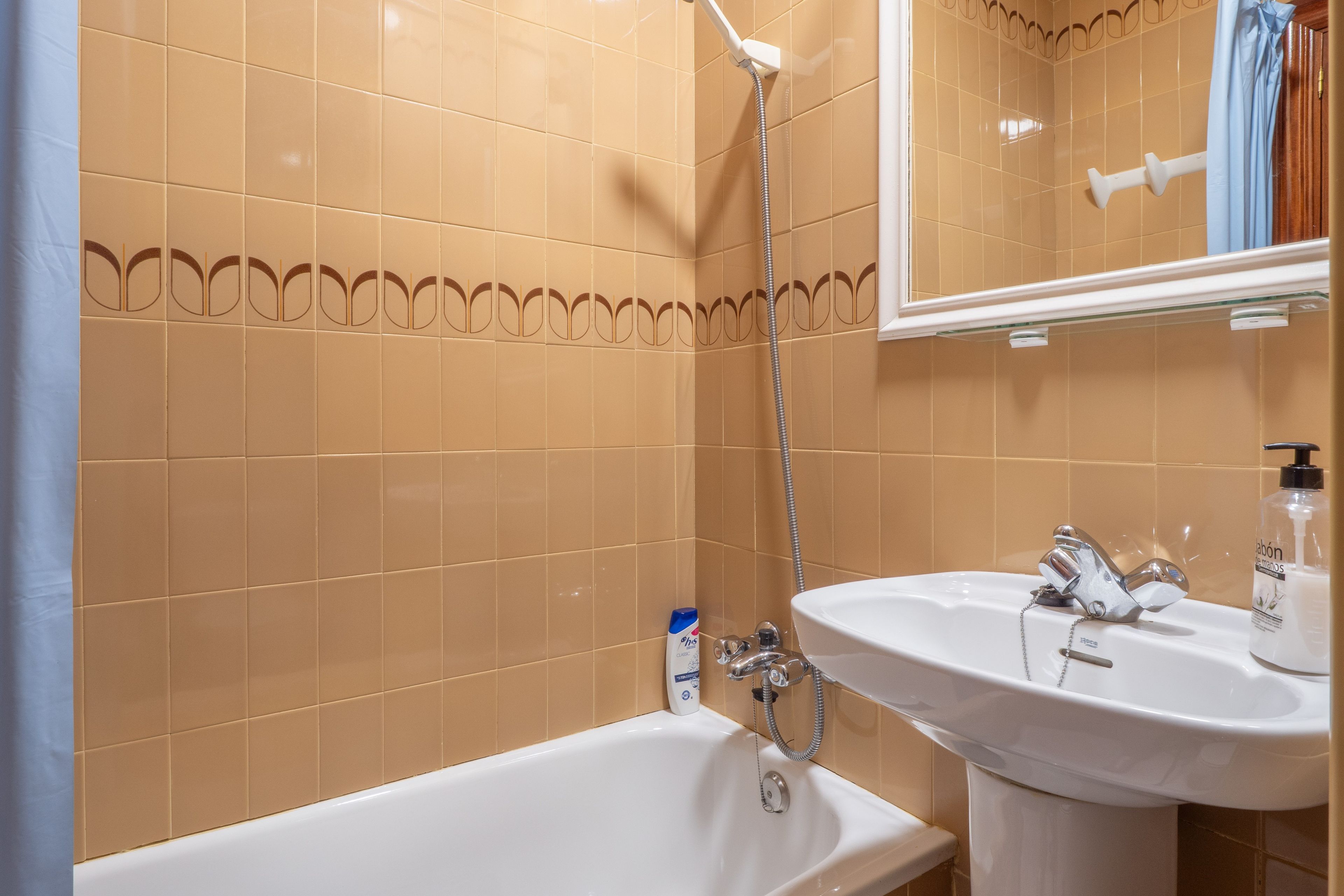 Un baño con paredes de azulejos color beige, una bañera blanca y un lavamanos blanco con un espejo encima.