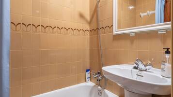 Un baño con paredes de azulejos color beige, una bañera blanca y un lavamanos blanco con un espejo encima.