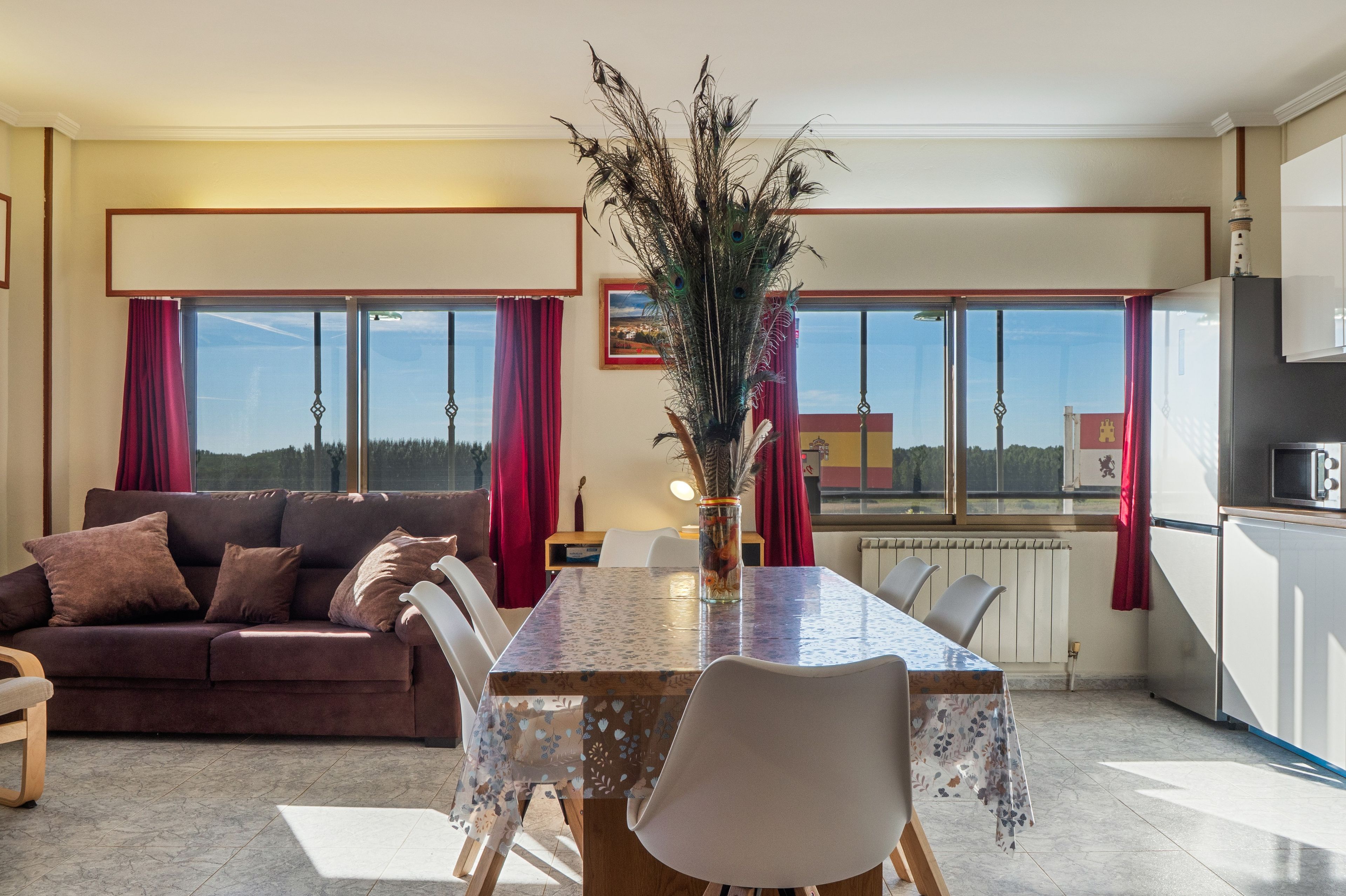 A modern living room with a sofa, dining table, chairs, and a view through large windows.