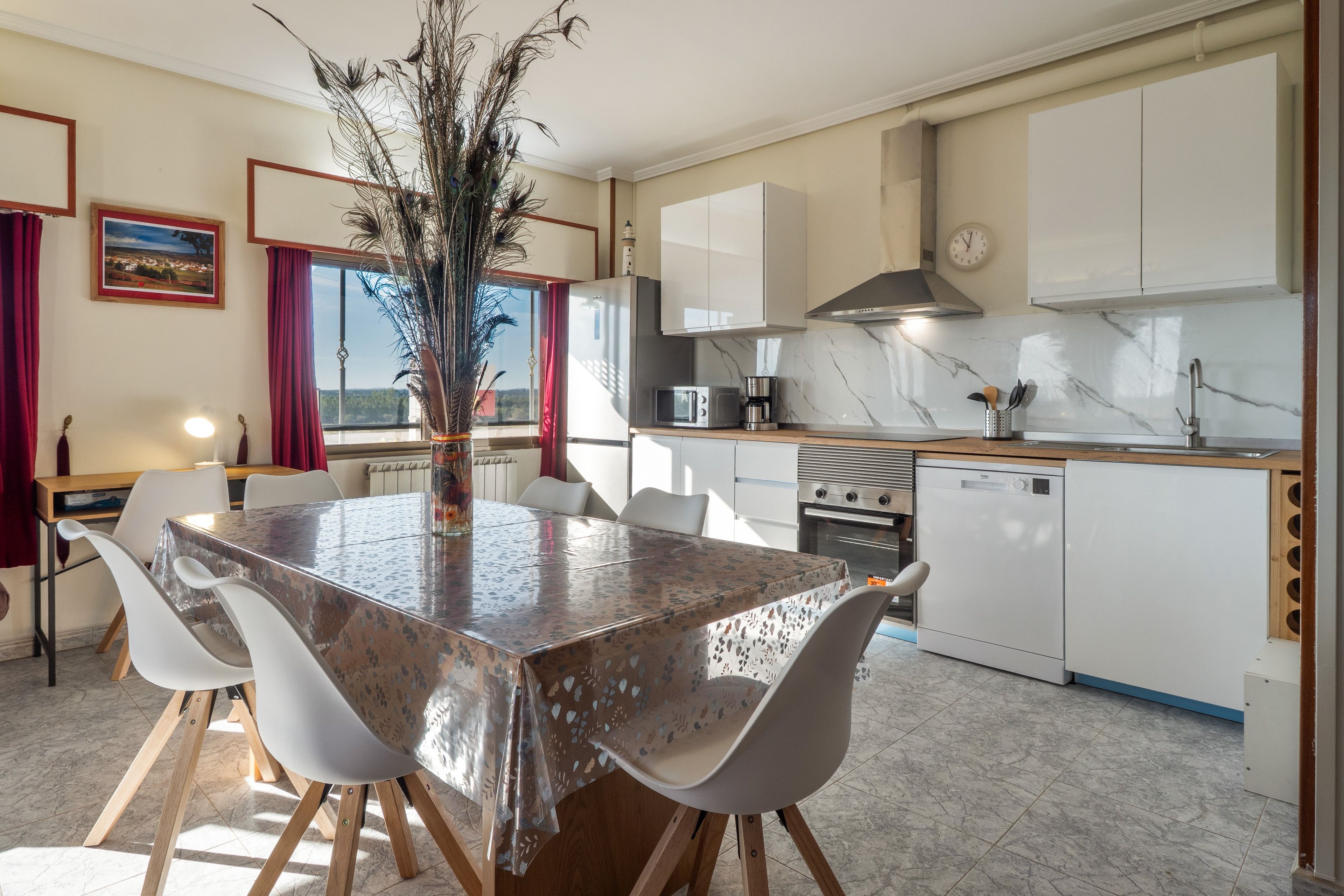 A modern kitchen with white cabinets, a dining table with chairs, and a decorative plant centerpiece.