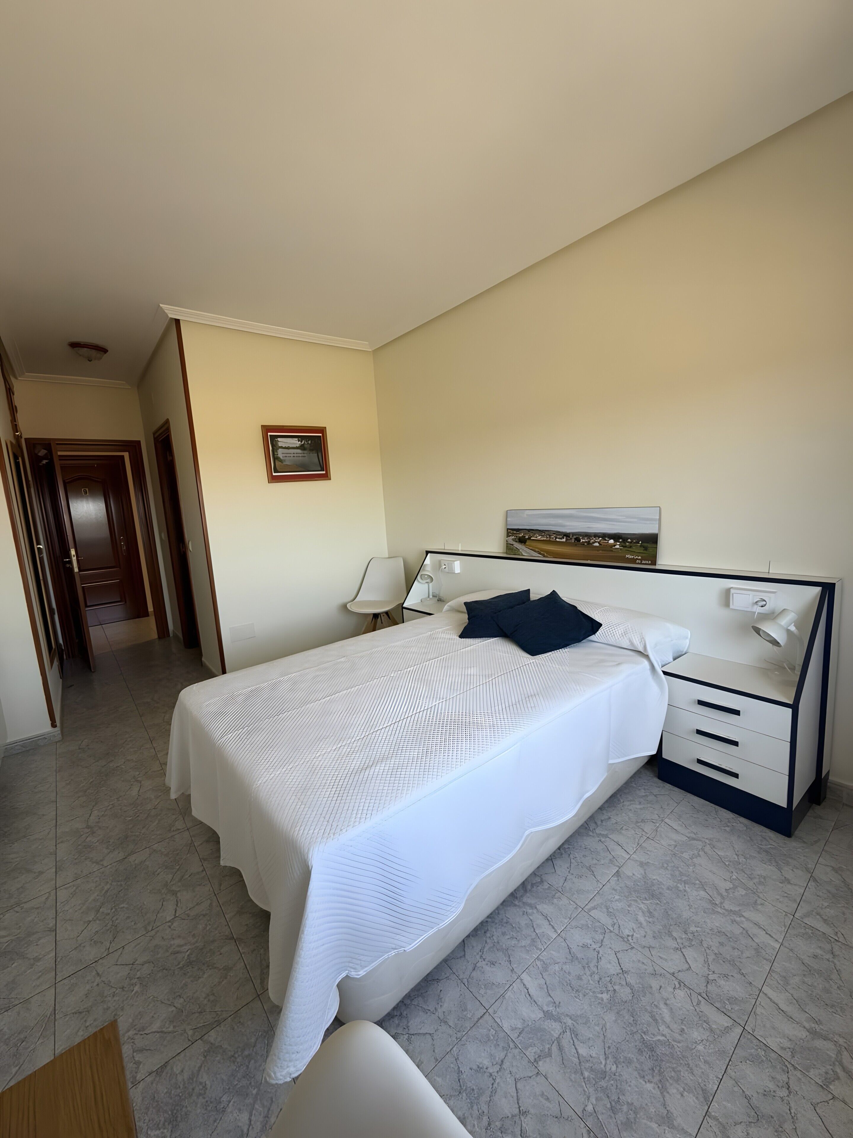 A hotel room with a large bed, bedside tables, a nightstand, and a framed picture on the wall.