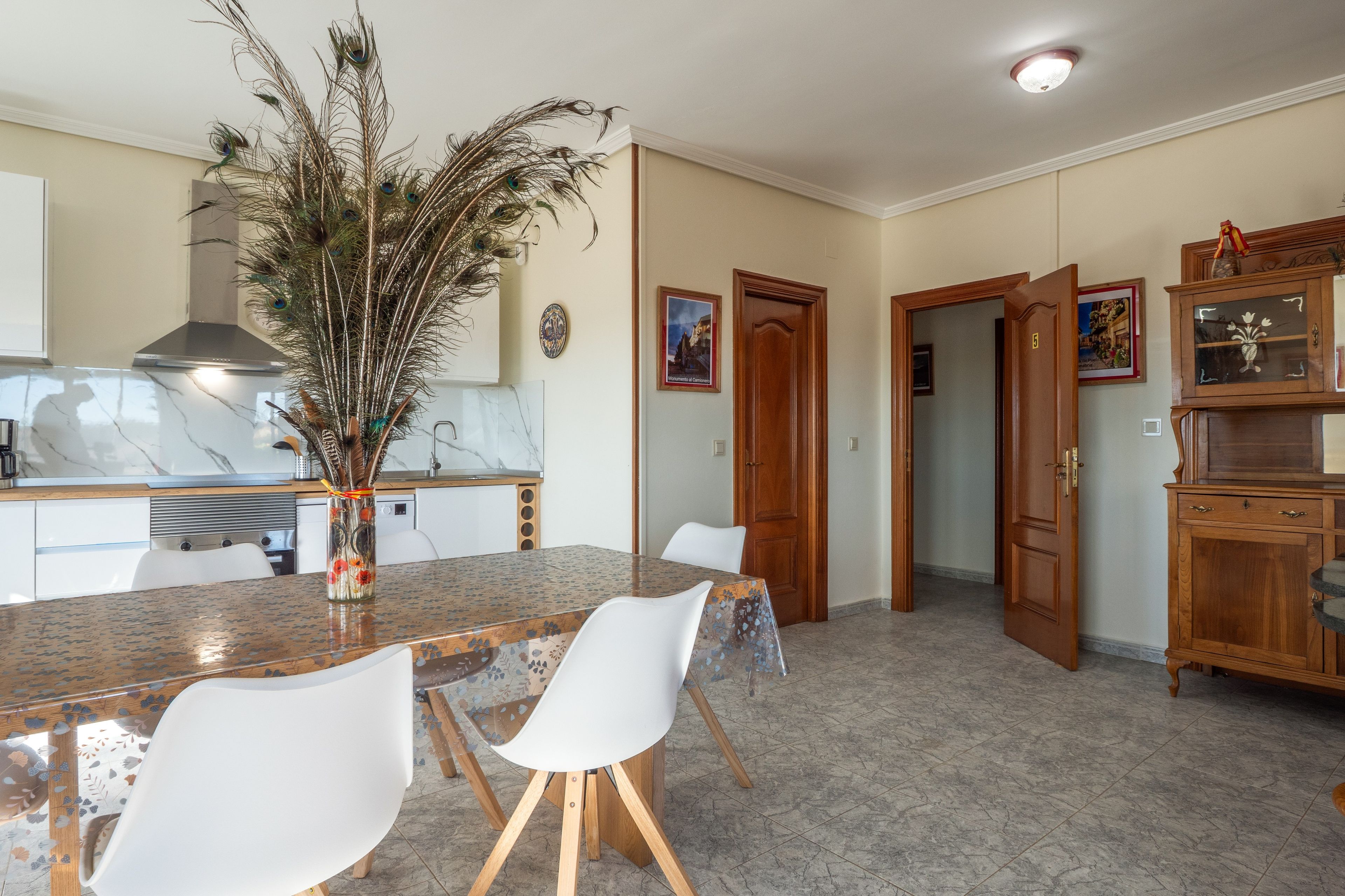 Una cocina moderna con encimera de mármol, una mesa de comedor con sillas y una decoración con plumas de pavo real.