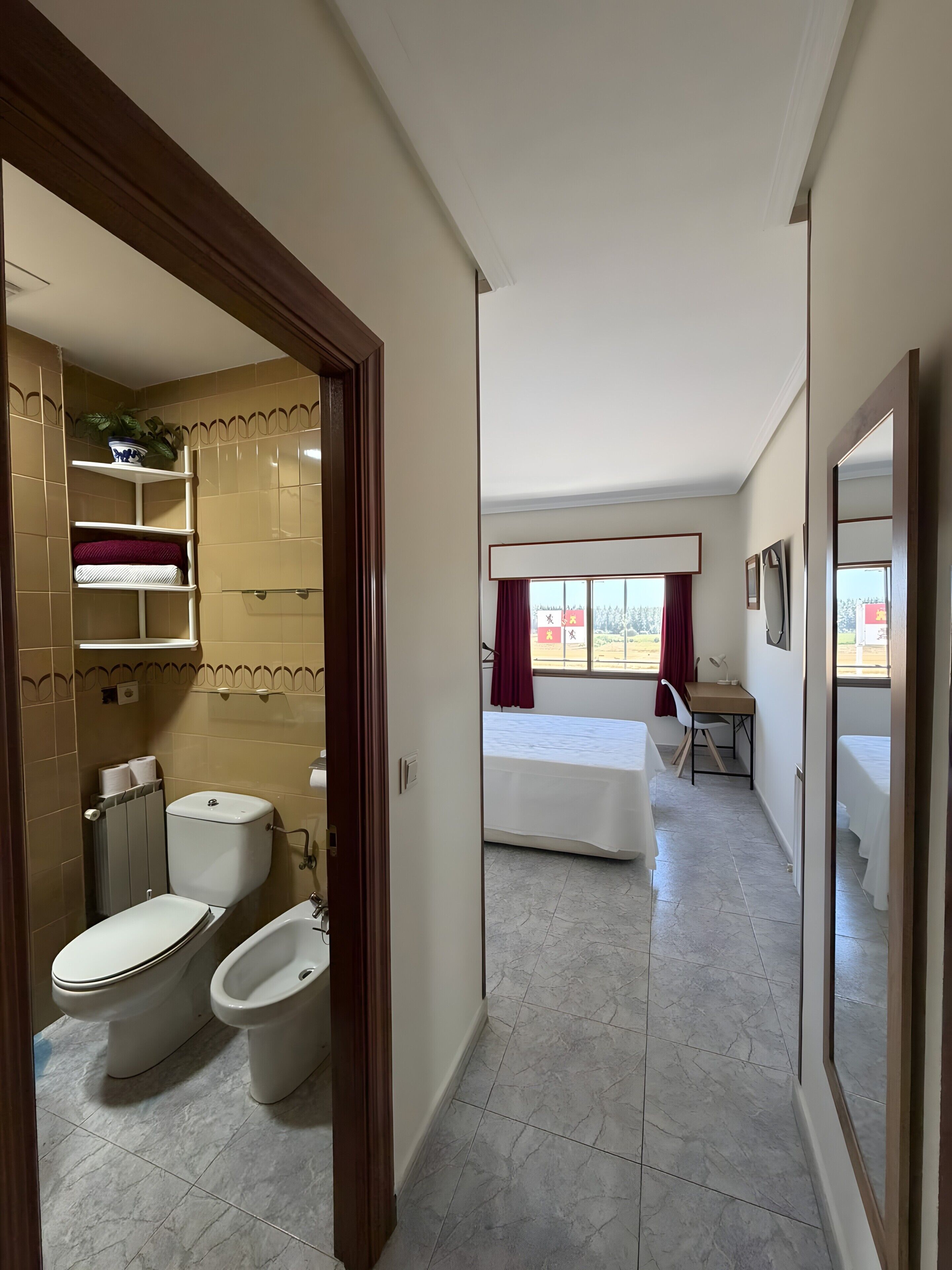 Una habitación de hotel con baño, una cama, un escritorio y una ventana con cortinas.