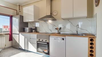 Una cocina moderna con gabinetes blancos, horno empotrado, lavavajillas y pileta de acero inoxidable.