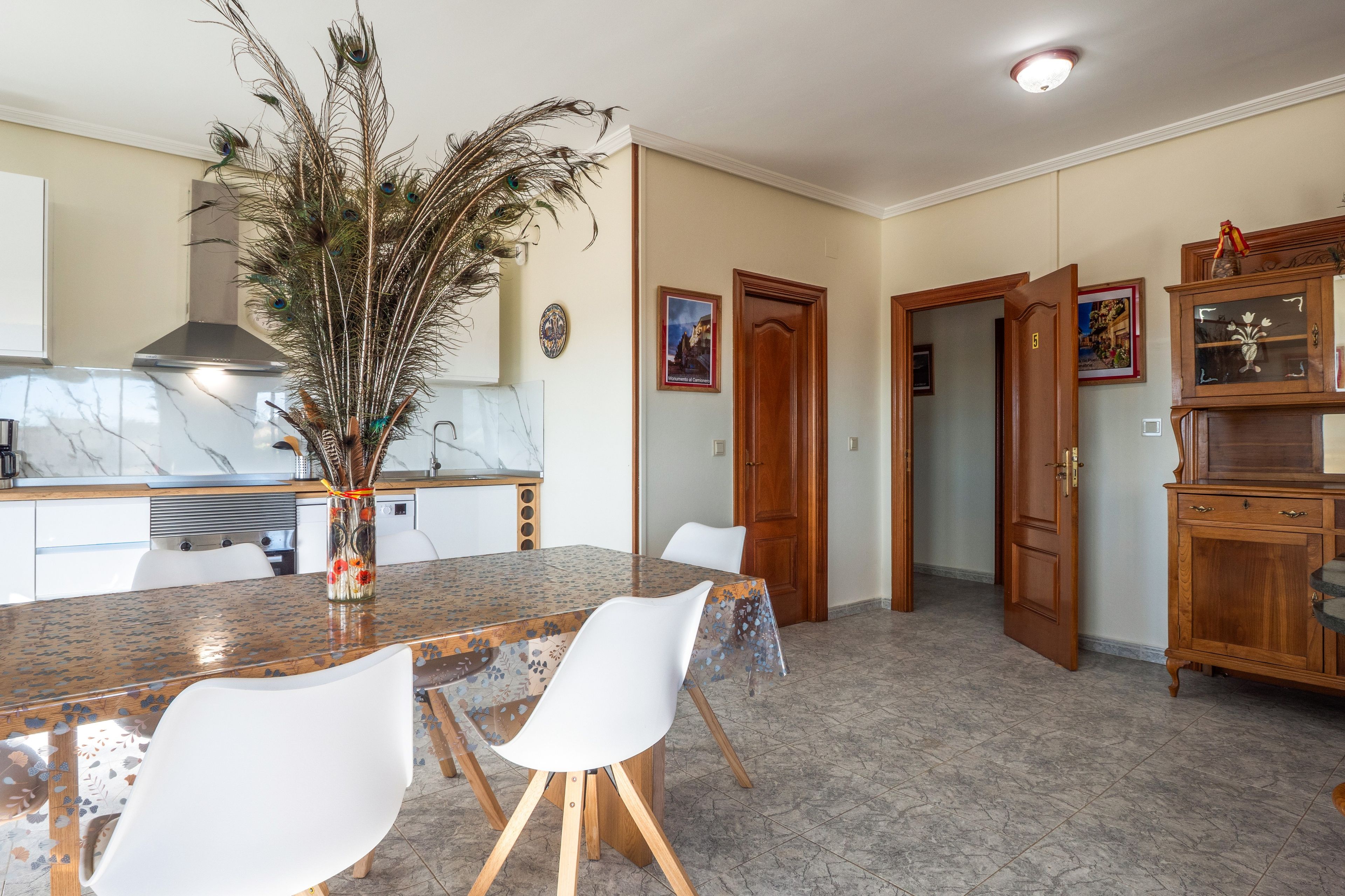 Une cuisine moderne dotée d’un plan de travail en marbre, d’une table à manger avec des chaises et d’un arrangement décoratif de plumes de paon.
