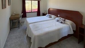 Un dormitorio con dos camas, un escritorio, una ventana con cortinas y una mesita de noche.