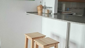 A kitchen with a white countertop, two wooden stools, a decorative plant, and a cabinet with glass doors. - Your home in Altea! 200 m from the beach / bright / 2 bedrooms / fully equipped / beautifully decorated. (Altea)