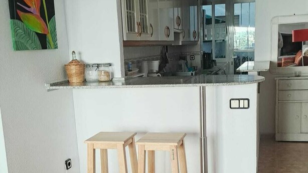 A modern kitchen with white cabinets, a central island with stools, and a colorful abstract painting on the wall. - Your home in Altea! 200 m from the beach / bright / 2 bedrooms / fully equipped / beautifully decorated. (Altea)