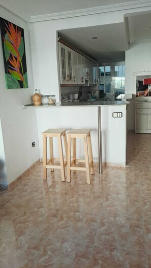 A modern kitchen with white cabinets, a central island with stools, and a colorful abstract painting on the wall. - Your home in Altea! 200 m from the beach / bright / 2 bedrooms / fully equipped / beautifully decorated. (Altea)