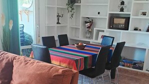 A living room with a sofa, dining table, chairs, and a kitchen area with shelves and a hanging light fixture. - Your home in Altea! 200 m from the beach / bright / 2 bedrooms / fully equipped / beautifully decorated. (Altea)