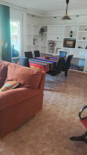 A living room with a sofa, dining table, chairs, and a kitchen area with shelves and a hanging light fixture. - Your home in Altea! 200 m from the beach / bright / 2 bedrooms / fully equipped / beautifully decorated. (Altea)