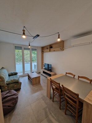 Ein gemütlicher, kompakter Wohnbereich mit Sofa, Esstisch und Stühlen, Fernseher und einer kleinen Küchenzeile.