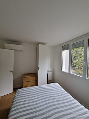 Quarto com cama, escada de madeira, guarda-roupa branco e janela com vista para árvores.