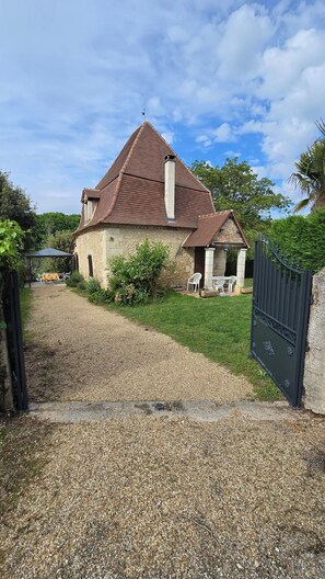 A stone house with a tiled roof, a gravel driveway, and a gated entrance. - Vacation Rental in France: Weekly Rentals with a Private Pool (La Jemaye-Ponteyraud)