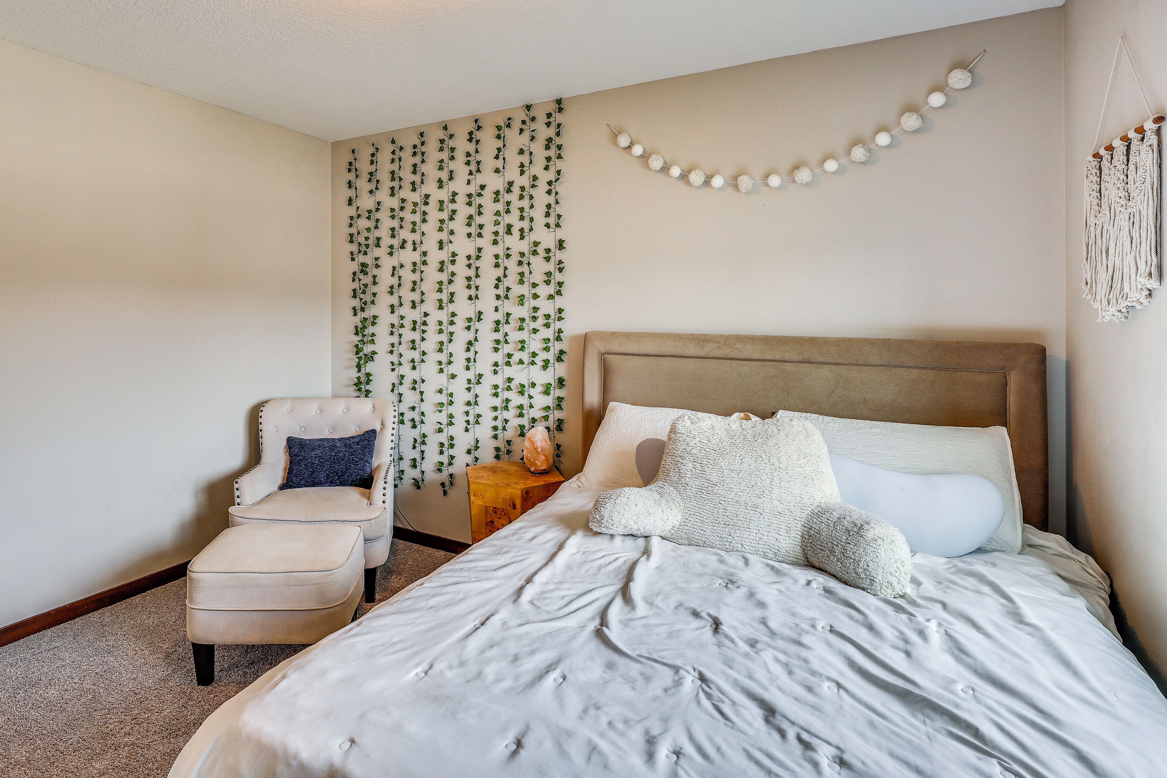 A bedroom with a bed, a chair, and a wall-mounted macrame piece.