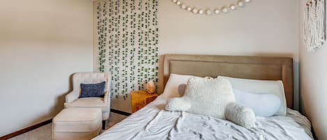 A bedroom with a bed, a chair, and a wall-mounted macrame piece.