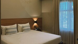 A hotel room with a large bed, a nightstand, a wall-mounted lamp, and a window with curtains. - Patio By Balai Norte La Union (San Juan)