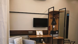 A hotel room with a bed, a sofa, a desk with a flat-screen TV, a wardrobe, and a shoe rack. - Patio By Balai Norte La Union (San Juan)