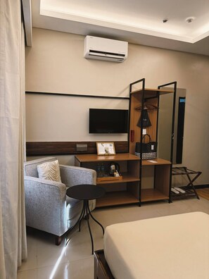 A hotel room with a bed, a sofa, a desk with a flat-screen TV, a wardrobe, and a shoe rack. - Patio By Balai Norte La Union (San Juan)