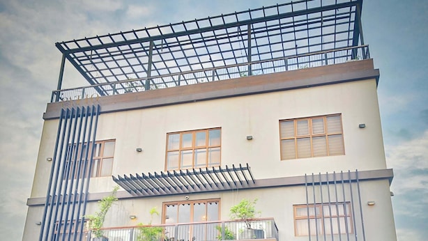 A multi-story hotel with a modern design, featuring a covered outdoor seating area and a prominent entrance with a logo. - Patio By Balai Norte La Union (San Juan)
