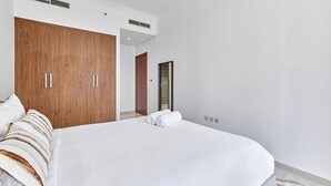 A bedroom with a large bed, wooden wardrobe, and a door leading to another room. - bnbme - Dunya Tower - 1BR (Dubai)