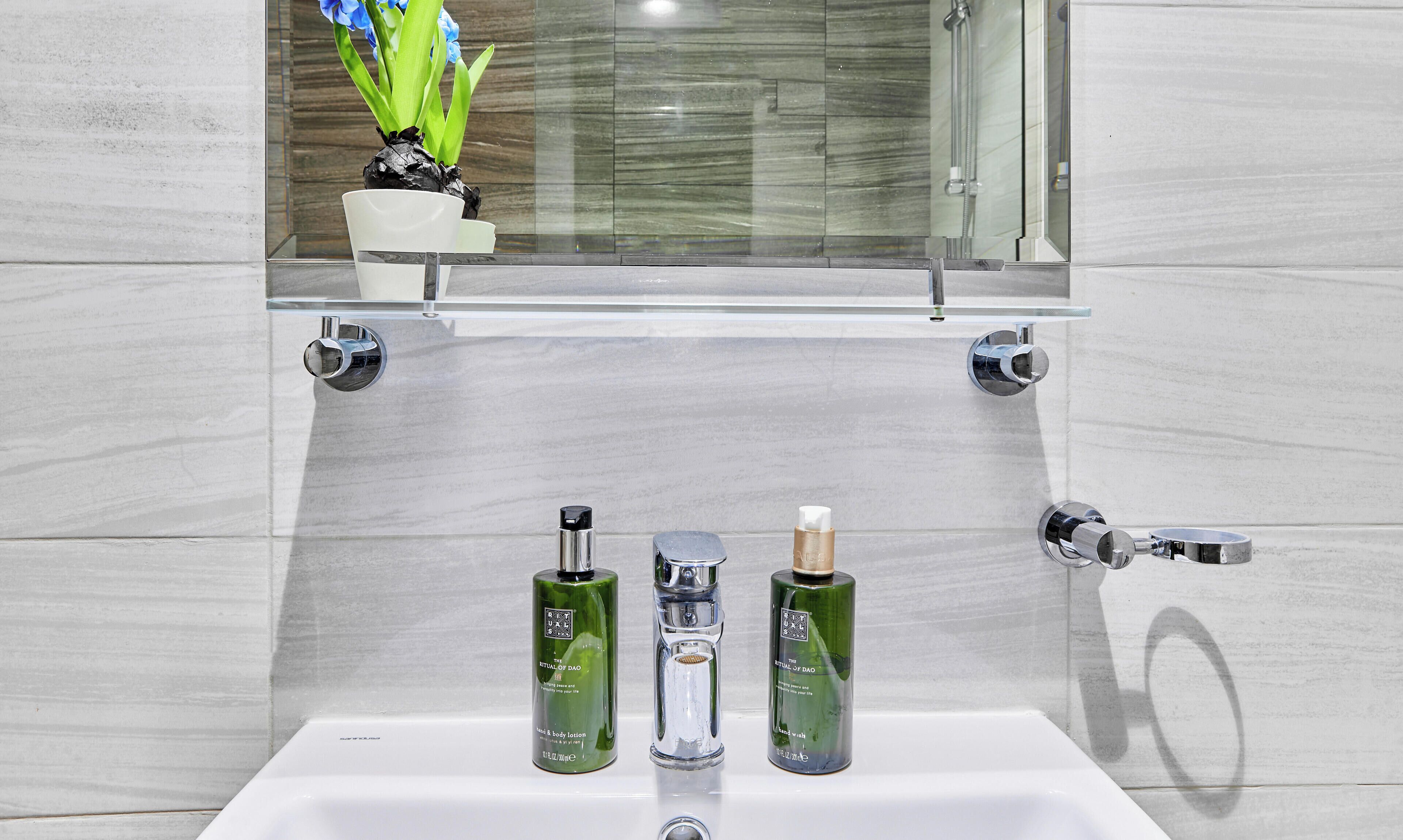 Ein Badezimmer mit einem weißen Waschbecken, zwei grünen Flaschen und einer klaren Glasablage darüber.