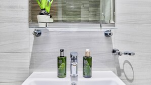A bathroom with a white sink, two green bottles, and a clear glass shelf above. - bnbme - Dunya Tower - 1BR (Dubai)