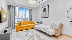 A modern hotel room with a sofa, bed, and a large window offering a city view. - bnbme - Dunya Tower - 1BR (Dubai)