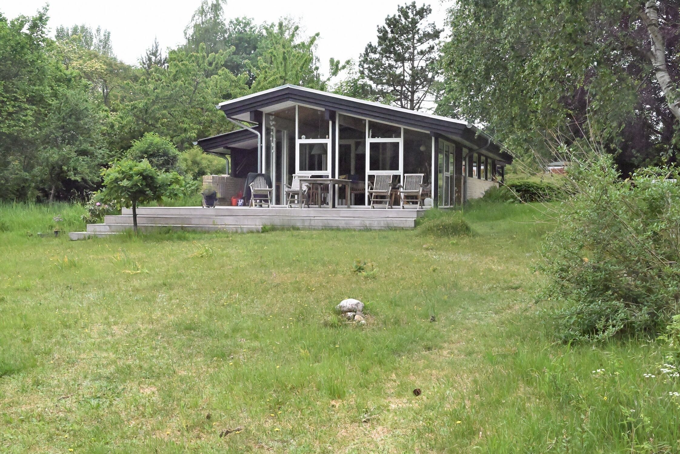 A modern house with a covered porch, surrounded by lush greenery.