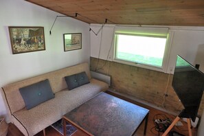Ein Zimmer mit einer Couch, einem Tisch, einem Fenster und zwei Bildern an der Wand.