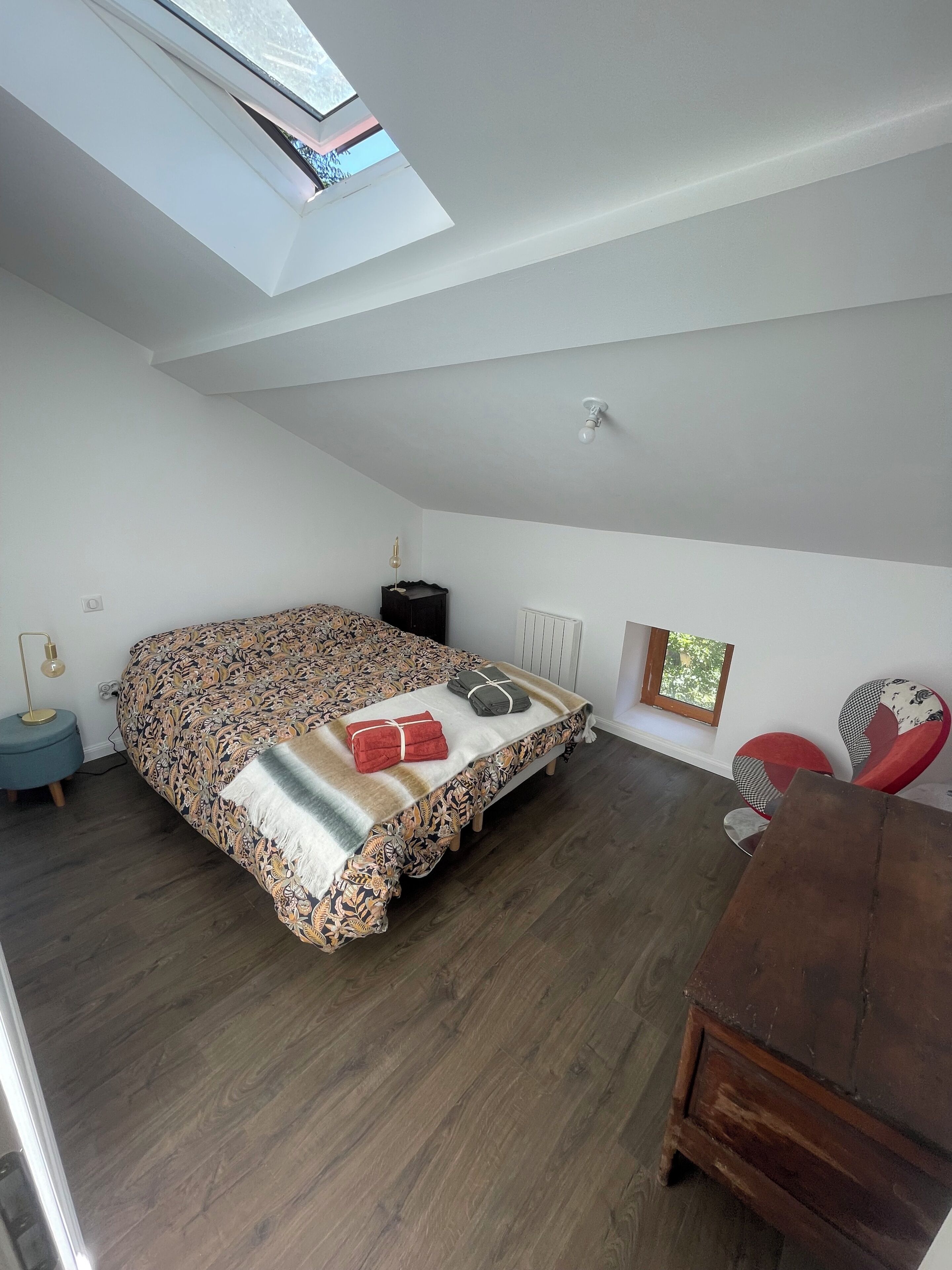 Ein Schlafzimmer mit einem Bett, einem Nachttisch, einer Lampe, einem Heizkörper und einem Fenster.