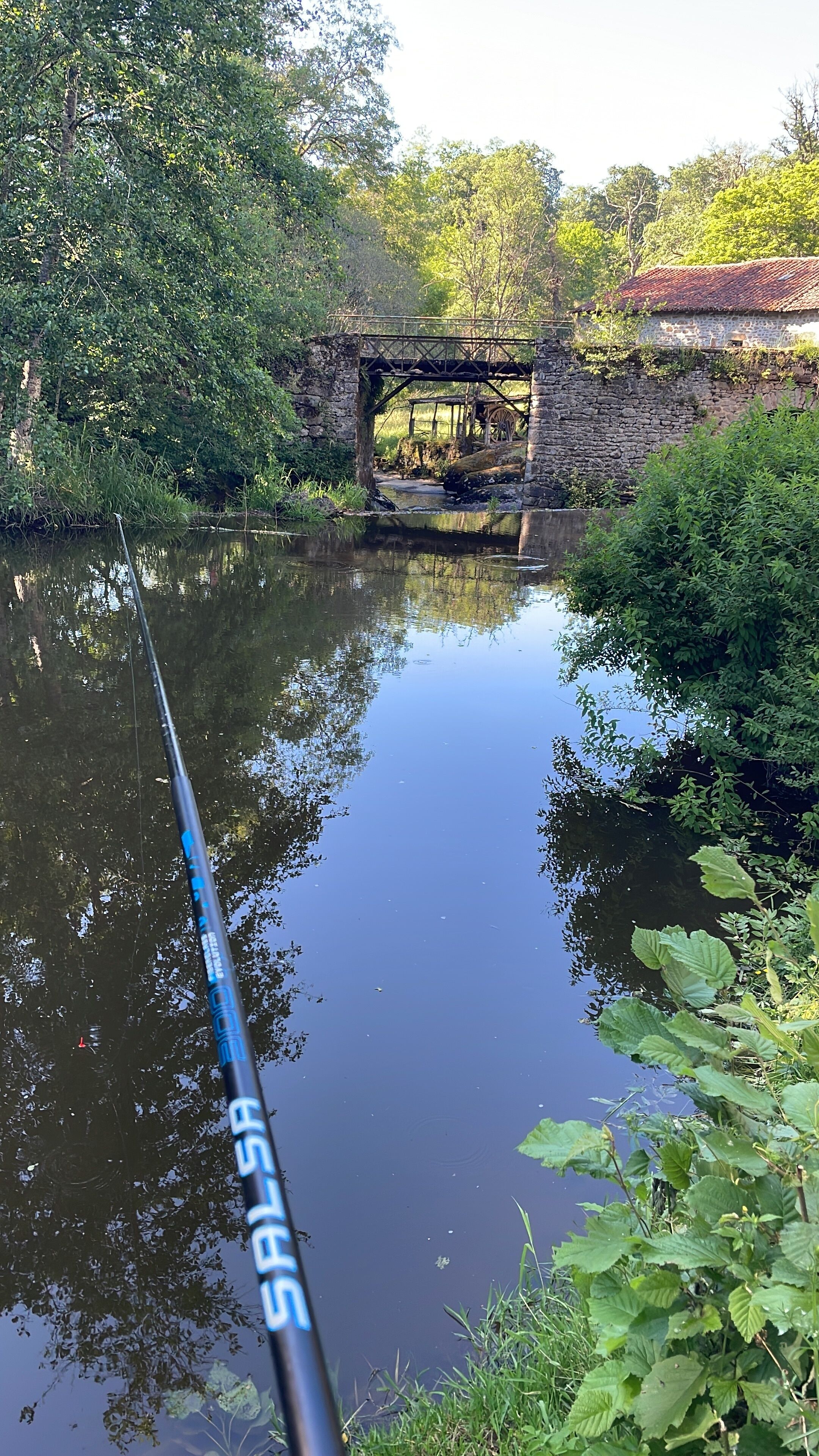 A fishing rod with a bridge and stone wall in the background.