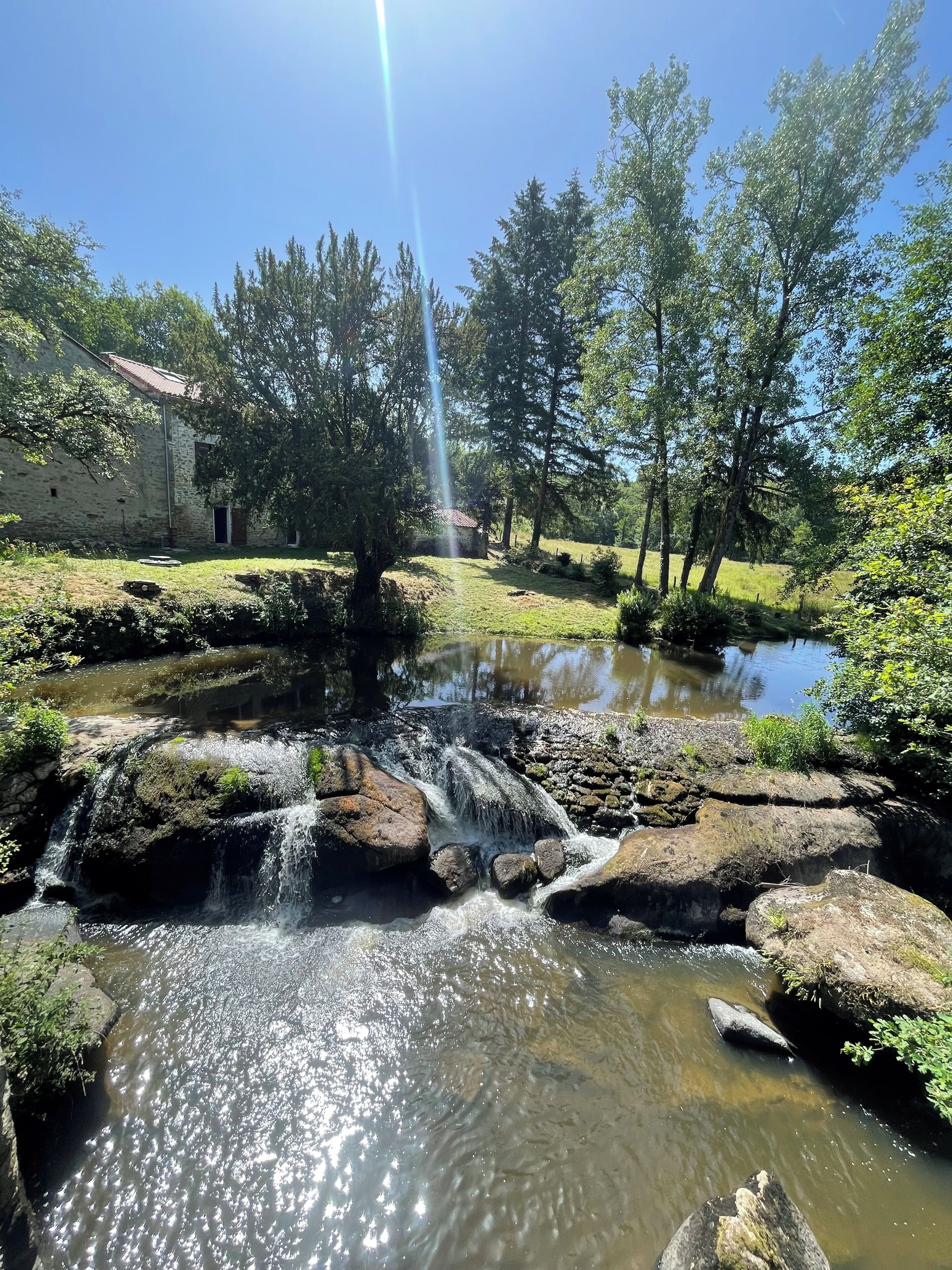 A natural landscape with a waterfall, a pond, and a stone building.