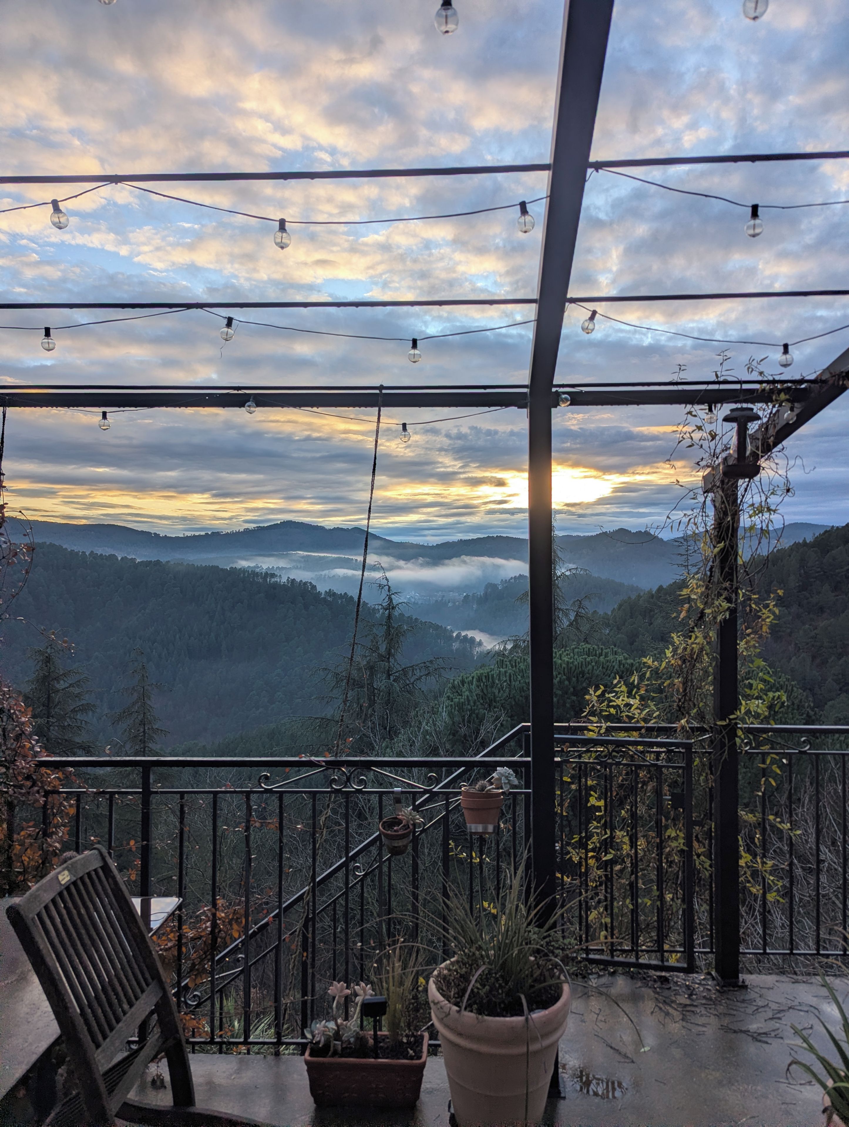 A balcony with a view of a mountainous landscape, potted plants, and a chair.