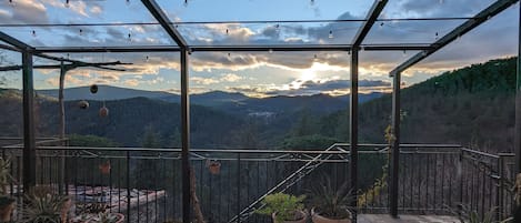 A covered outdoor area with a view of a mountainous landscape, potted plants, and string lights.
