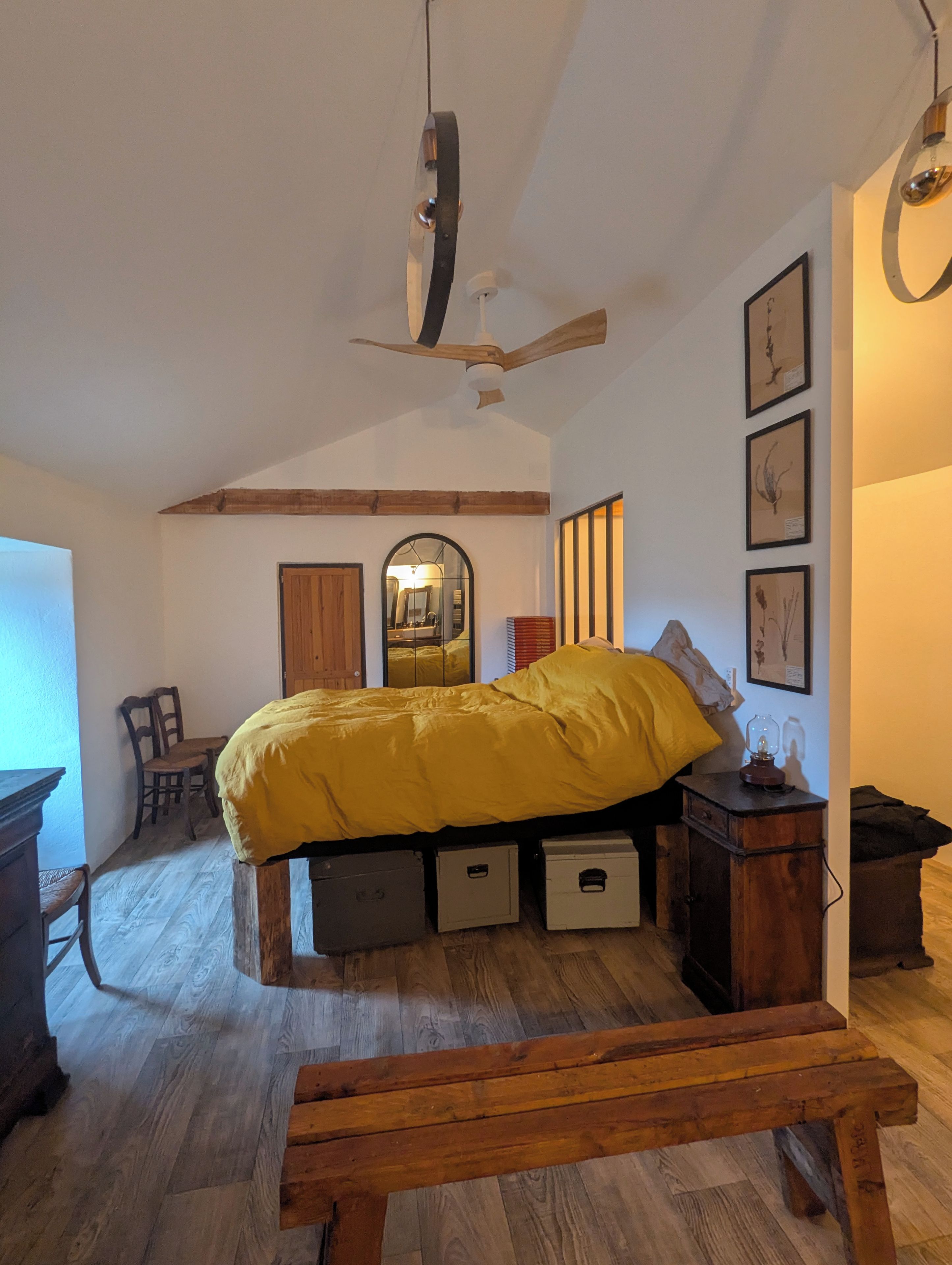 Een slaapkamer met een bed, houten vloer, een bankje, een bureau en een spiegel.