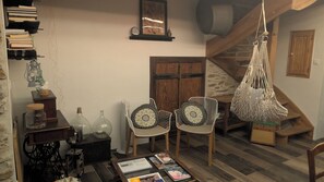A cozy room with a wooden floor, a bookshelf, two chairs with patterned cushions, a hanging macrame bag, and a wooden door.