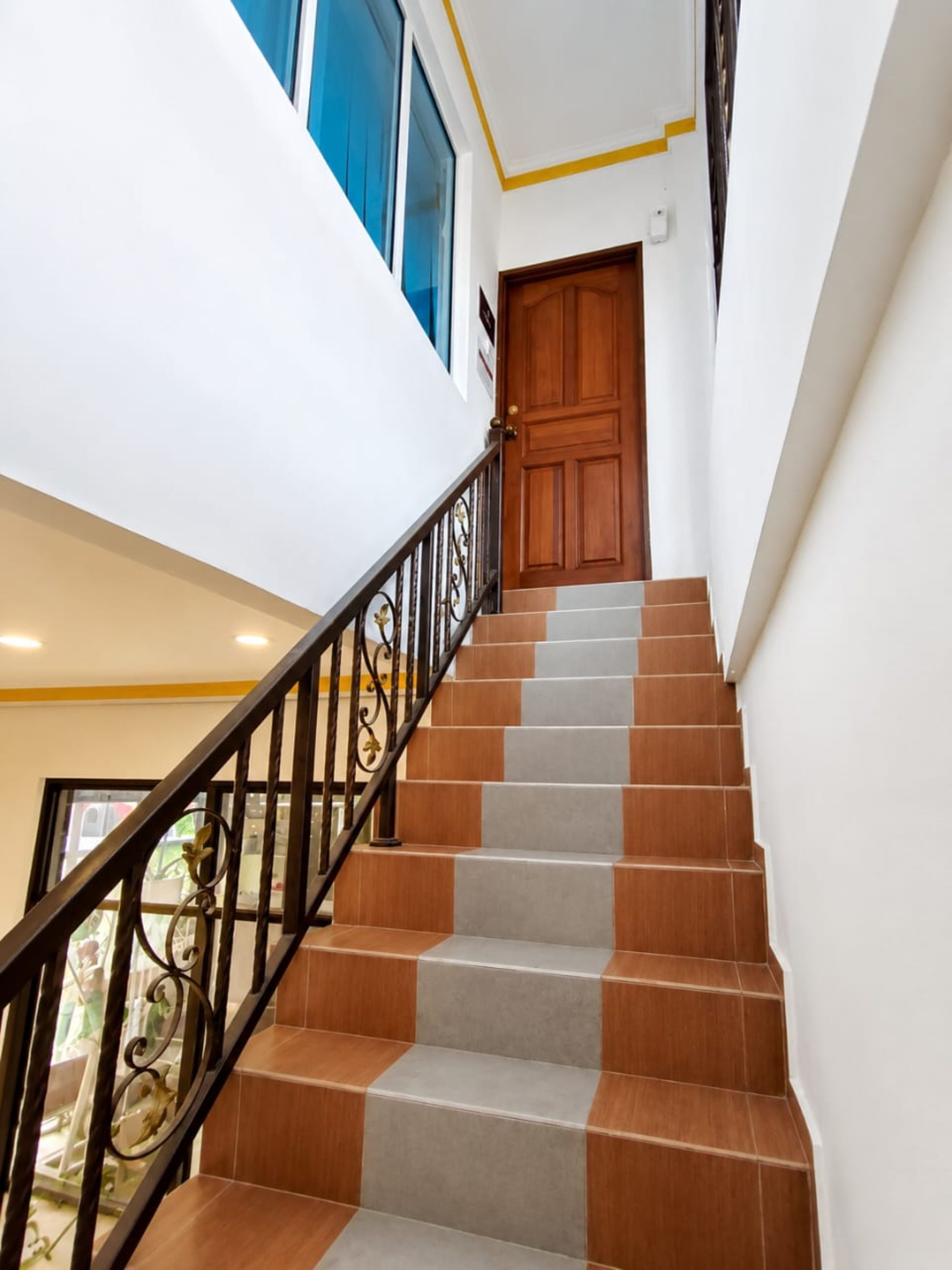 A staircase with alternating brown and grey steps, a wooden door at the top, and a black metal railing.