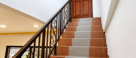 A staircase with alternating brown and grey steps, a wooden door at the top, and a black metal railing.