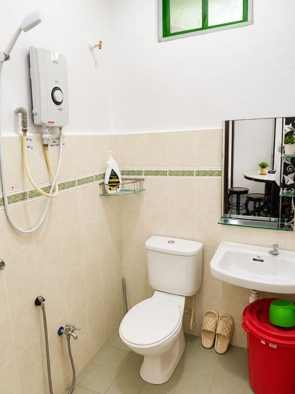 Une salle de bain comprenant des toilettes, un lavabo, une douchette à main et une étagère en verre où sont rangés les articles de toilette.
