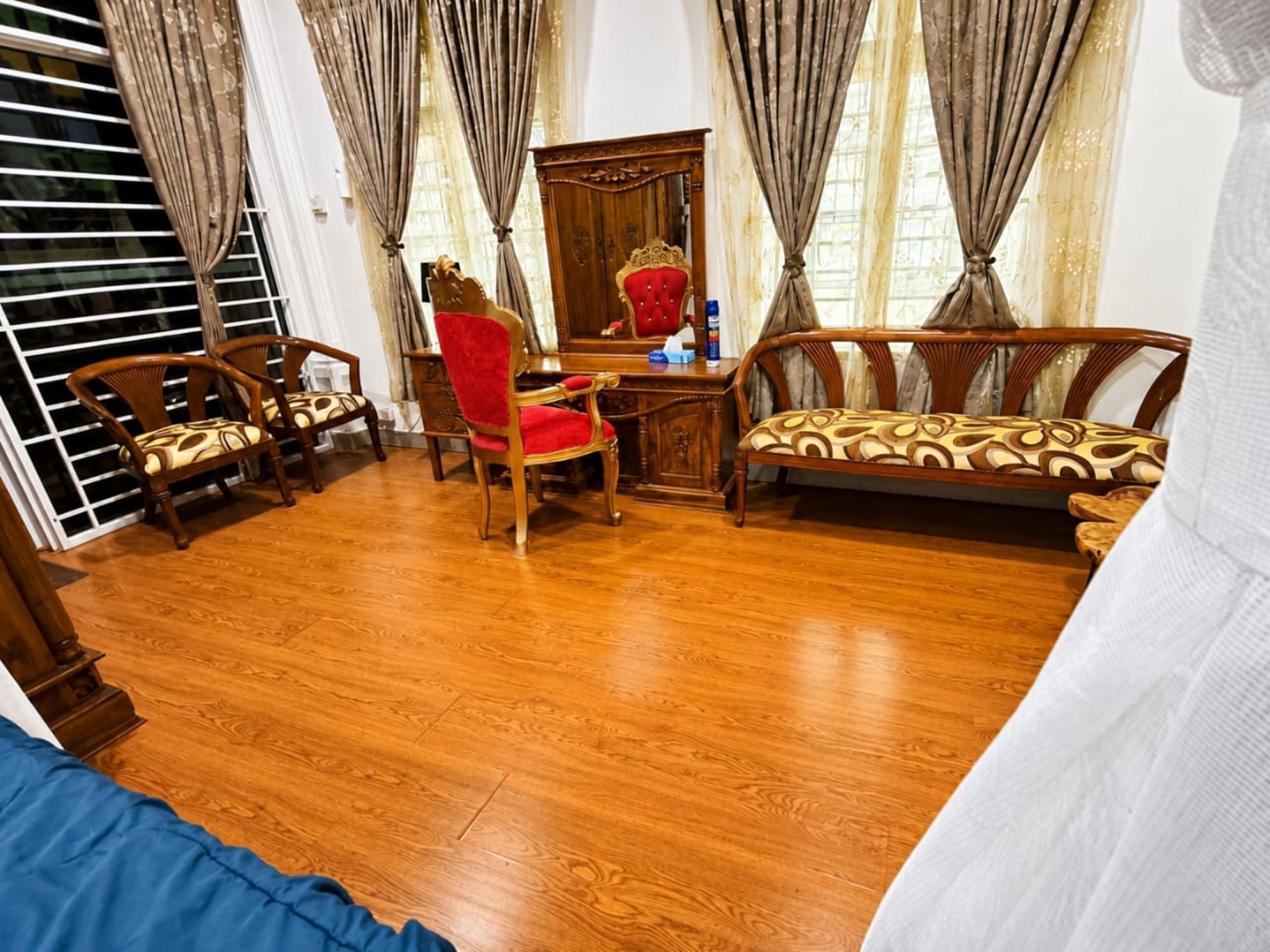 A room with a wooden floor, a red chair, a wooden sofa, and a desk with a mirror.