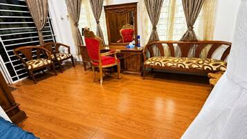 A room with a wooden floor, a red chair, a wooden sofa, and a desk with a mirror.