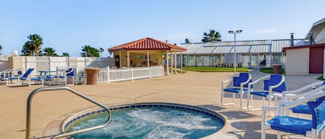 A pool area with lounge chairs, a hot tub, and a covered seating area.