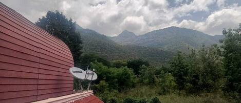 A red-roofed building with a satellite dish, surrounded by lush greenery and mountains in the background.