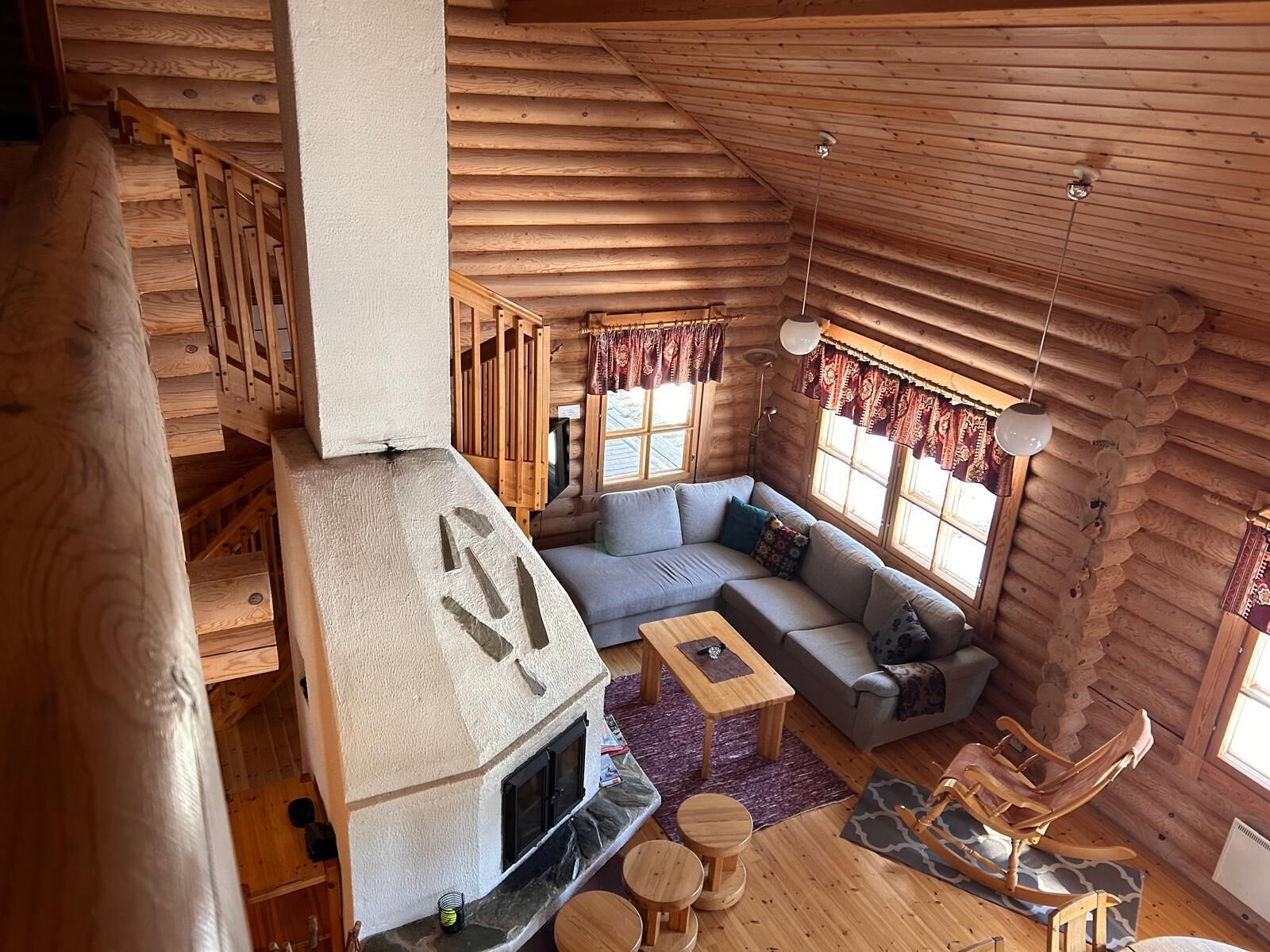 Interior de una cabaña de madera con chimenea, un sofá, una mecedora y una escalera.
