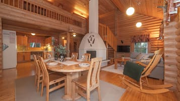 Interior de una cabaña de troncos con comedor, chimenea, sofá y mecedora.