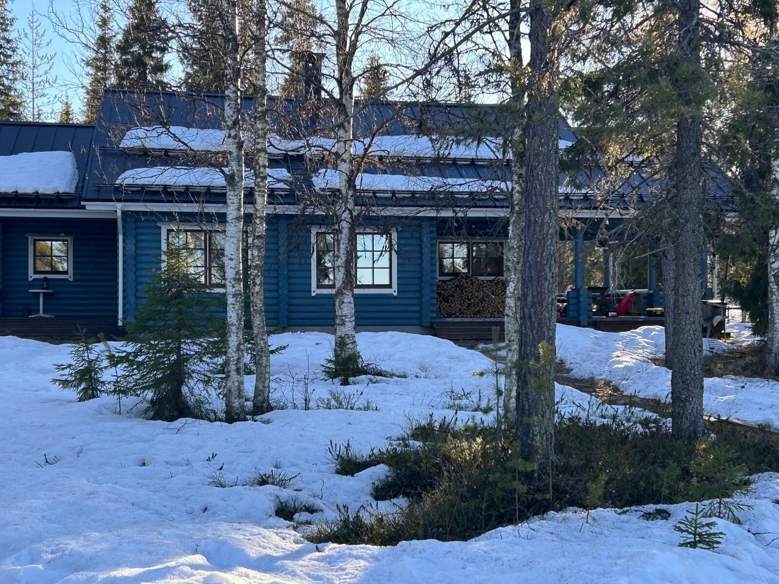 Lumipeitteinen mökki, jonka ympärillä on puita ja lumista maisemaa.