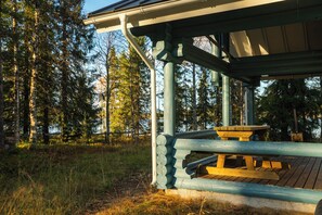 A wooden picnic shelter with a bench, surrounded by a forest.