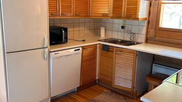 Une cuisine compacte avec des meubles en bois, un réfrigérateur, un four à micro-ondes, un évier et une fenêtre avec un rideau.