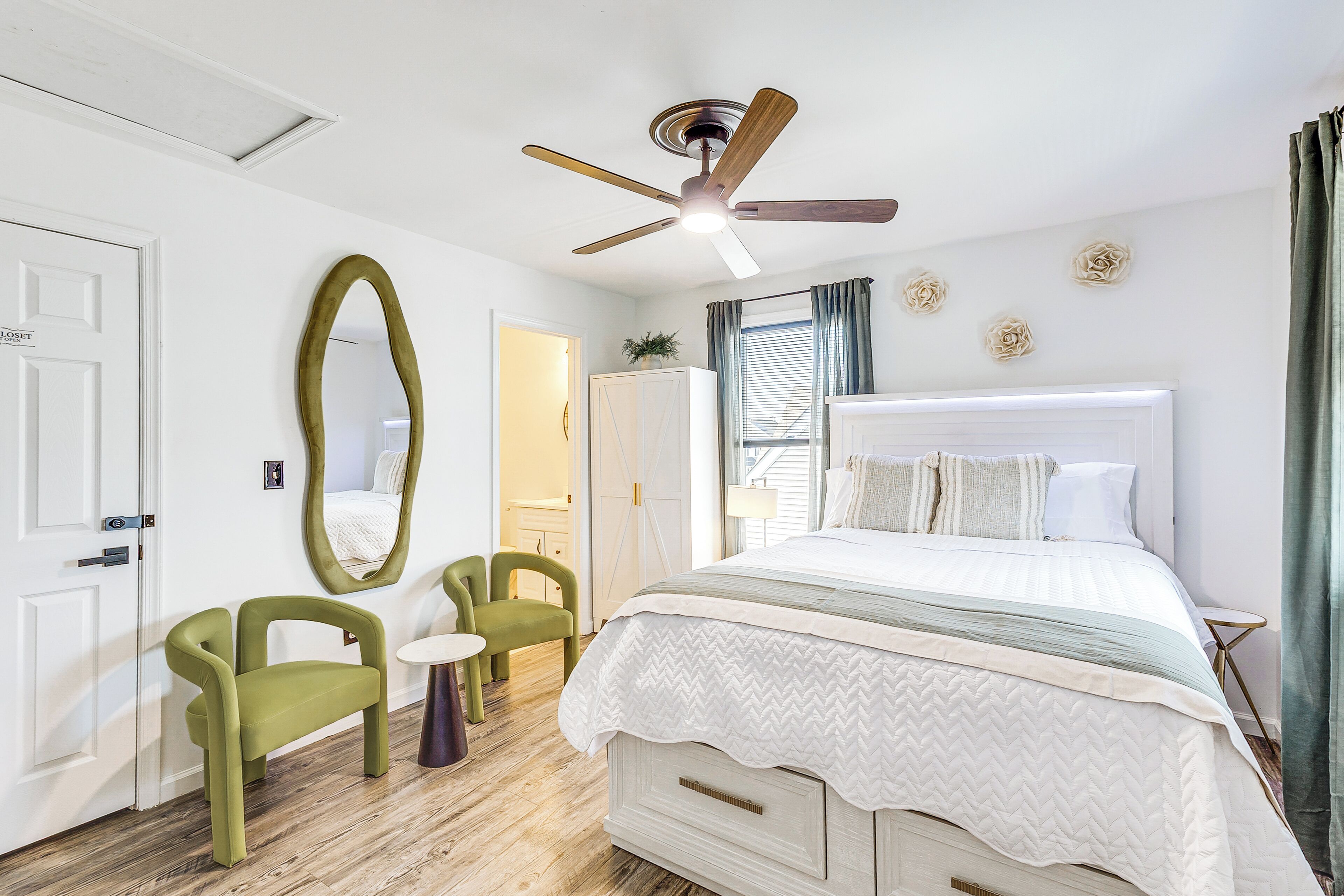 A bedroom with a bed, a ceiling fan, a large mirror, and a door.
